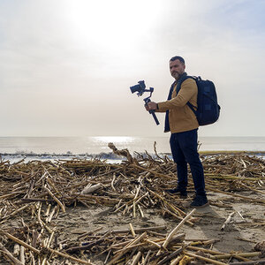 A climate journalist holding a camera, standing on ocean debris. A climate journalist holding a camera, standing on ocean debris.