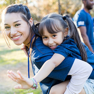 A young female volunteer has a smiling girl on her back while other volunteers in the background look on. A young female volunteer has a smiling girl on her back while other volunteers in the background look on.