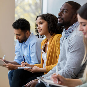 A group of men and women taking notes at a meeting. A group of men and women taking notes at a meeting.