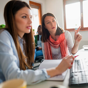 Two women in an office work in front of a computer.