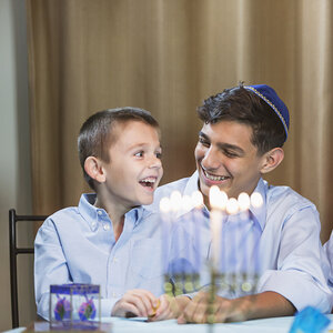 A teen and a young boy sitting at a dinner table with a menorah in the foreground. A teen and a young boy sitting at a dinner table with a menorah in the foreground.