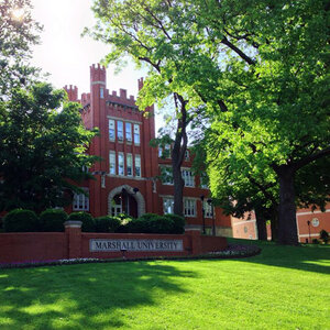 A red brick college building surrounded by trees with a sign that reads: Marshall University. A red brick college building surrounded by trees with a sign that reads: Marshall University.