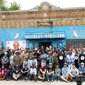 A large group of people in front of the light blue façade of an old jazz club with a sign that reads: The Blue Bird Inn. A large group of people in front of the light blue façade of an old jazz club with a sign that reads: The Blue Bird Inn.