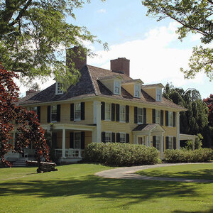 A colonial era manor house on lawn surrounded by trees - an image of Sylvester Manor.