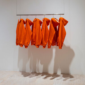 An art installation of orange hoodie sweatshirts hanging on a rack to create shadows suggesting the bodies of prisoners.