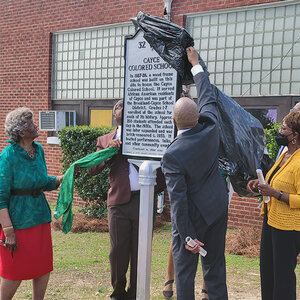 A group of African American men and women unveiling a historic marker on a school campus.