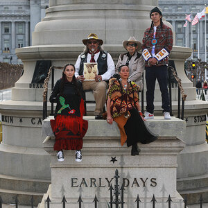 A group of Indigenous people sitting on the base of a monument. A group of Indigenous people sitting on the base of a monument.