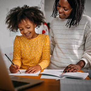 An African American mother watches her daughter draw a picture.