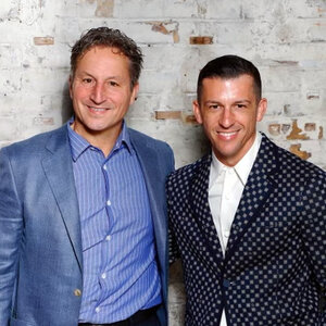 Two men wearing sport jackets pose for a photo in front of a painted brick wall - David Herro and Jay Franke.