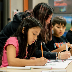 A young girl in a pink top using a pencil works on a class assignment.