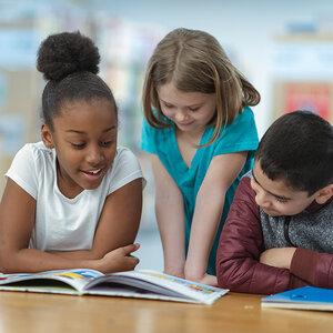Three children at a library table reading to each other from a book. Three children at a library table reading to each other from a book.