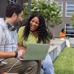 Two smiling college students with a laptop work together outside. Two smiling college students with a laptop work together outside.