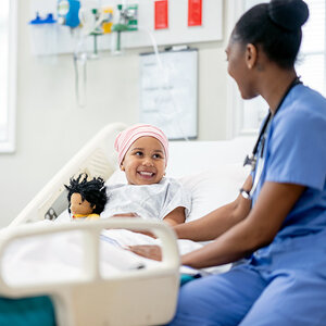 A young girl cancer patient is comforted by her African American female doctor.