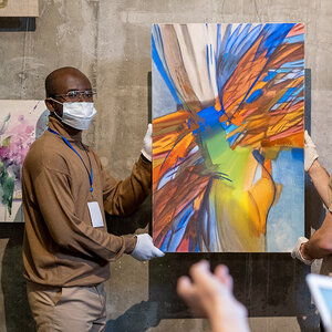 An art museum curator hangs a brightly colored abstract painting. An art museum curator hangs a brightly colored abstract painting.