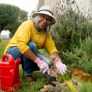 An older woman wearing a hat and gardenning gloves is watering her plants. An older woman wearing a hat and gardenning gloves is watering her plants.
