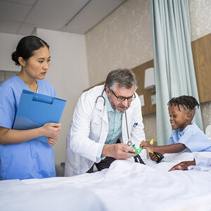A doctor and nurse check in on a smiling child in a hospital bed. A doctor and nurse check in on a smiling child in a hospital bed.