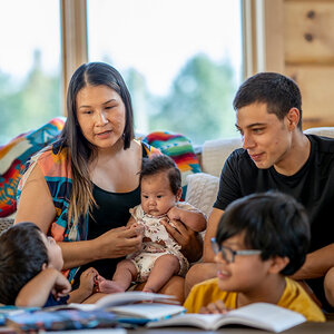 A family sits on a couch at home while the children do their homework. A family sits on a couch at home while the children do their homework.