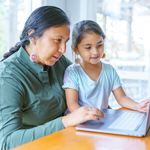 A Native American mother works on her computer with her child at hand. A Native American mother works on her computer with her child at hand.