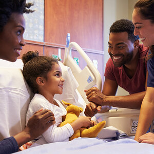 An African American mother and father tend to their child in a hospital bed.