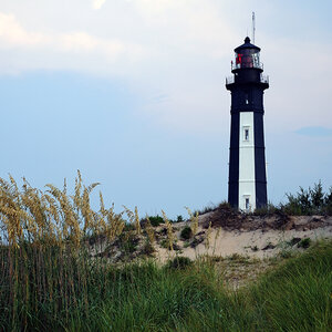 A lighthouse surrounded by sand dunes and shore grasses.