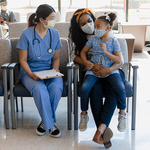 A female physician consults a mother and her daughter sitting in a hospital waiting room.