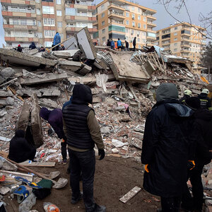 A group of people stand in front of a collapsed building following an earthquake.