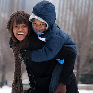 An African American mother carries her child on her back as they play in the snow. An African American mother carries her child on her back as they play in the snow.