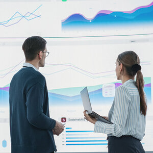 Two data scientists, a man and woman, review their work on a giant screen. Two data scientists, a man and woman, review their work on a giant screen.