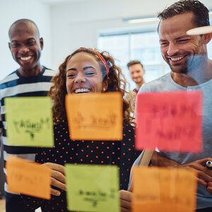 Business students review sticky notes on a glass wall during a brainstorming session.