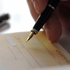 A closeup of a hand holding a foundation pen, about to sign a check. A closeup of a hand holding a foundation pen, about to sign a check.