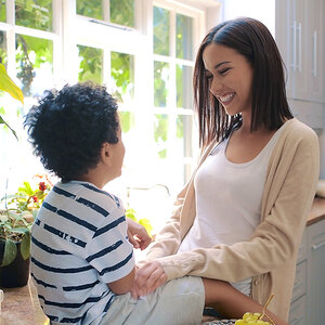 A mother and her toddler play in front of a sunlit window.