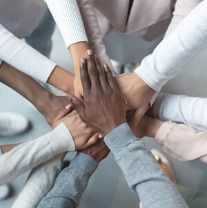 A closeup image of many people’s hands reaching into a circle to form a pile. A closeup image of many people’s hands reaching into a circle to form a pile.