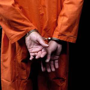 A man in an orange jumpsuit with a closeup of his hands handcuffed behind his back. A man in an orange jumpsuit with a closeup of his hands handcuffed behind his back.
