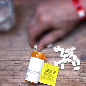 An open container of opioids, with several pills spilled on a table.