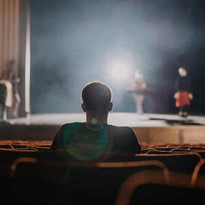A single spectator sits in a dark theater.