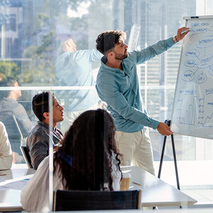 A group of business people in a conference room as a man draws on a chart on a board.