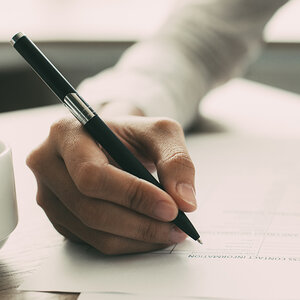 A close-up of a person’s hand holding a pen while the person completes a form.