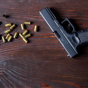 A handgun and several bullets lay on a wooden table.