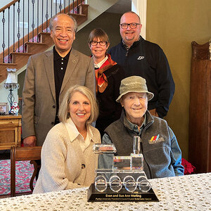 A group photo of five people standing and sitting behind a table, including Sue Ann (left) and Evan Werling (both seated).