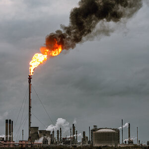 An oil refinery belches fire a black smoke into a gray sky.