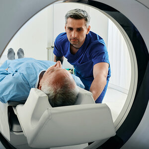 A hospital technician guides a patient into a CT scanner. A hospital technician guides a patient into a CT scanner.
