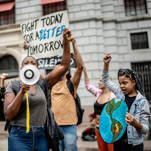 An African American woman speaks into a megaphone at a protest surrounded by people holding signs.