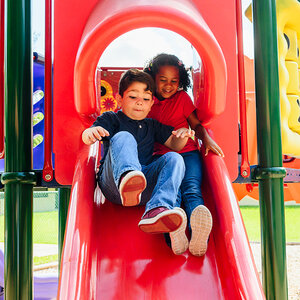 Two children playing on a playground slide.