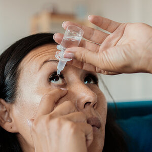 A woman is putting eye drops in her eye.