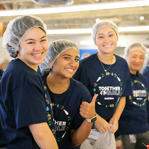 Volunteers in T-shirts and hair nets smile for the camera. Volunteers in T-shirts and hair nets smile for the camera.
