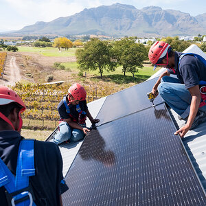 Workers install solar panels with farmland and mountains in the background. Workers install solar panels with farmland and mountains in the background.