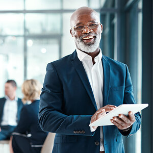 A Black businessman wearing a suit and holding a computer tablet.
