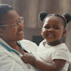 A female doctor holds a young girl who is grinning for the camera. A female doctor holds a young girl who is grinning for the camera.