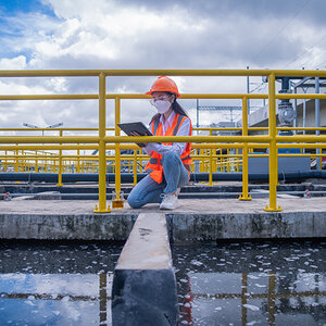 A woman wearing a mask takes notes while examining a wastewater treatment facility.