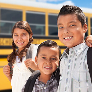 Latin-American school children pose for a photo in front of their yellow school bus.